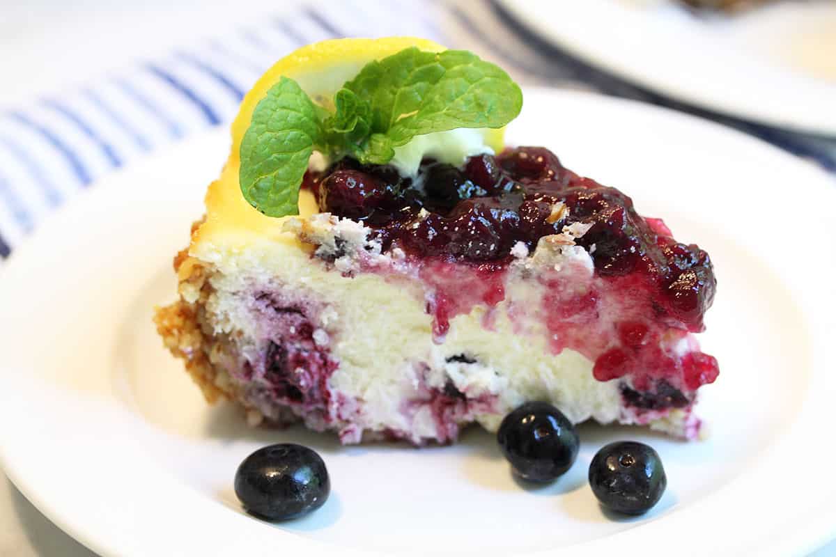 Closeup of single piece of cheesecake with lemon and mint on top.