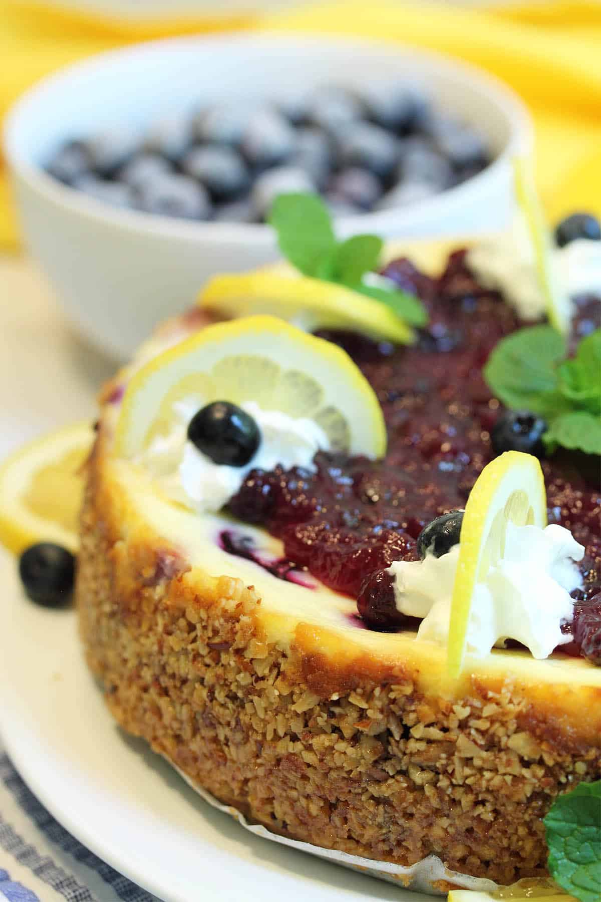 Side view of cheesecake with bowl of blueberries in background.