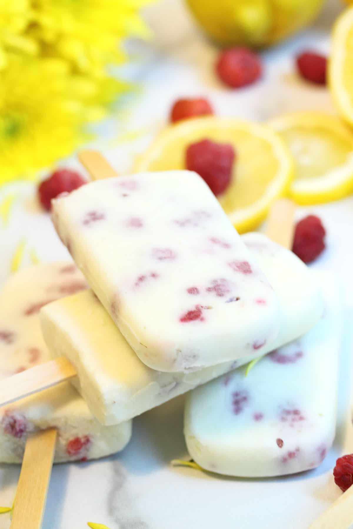 Closeup of stacked popsicles with sliced lemons and raspberries in background.