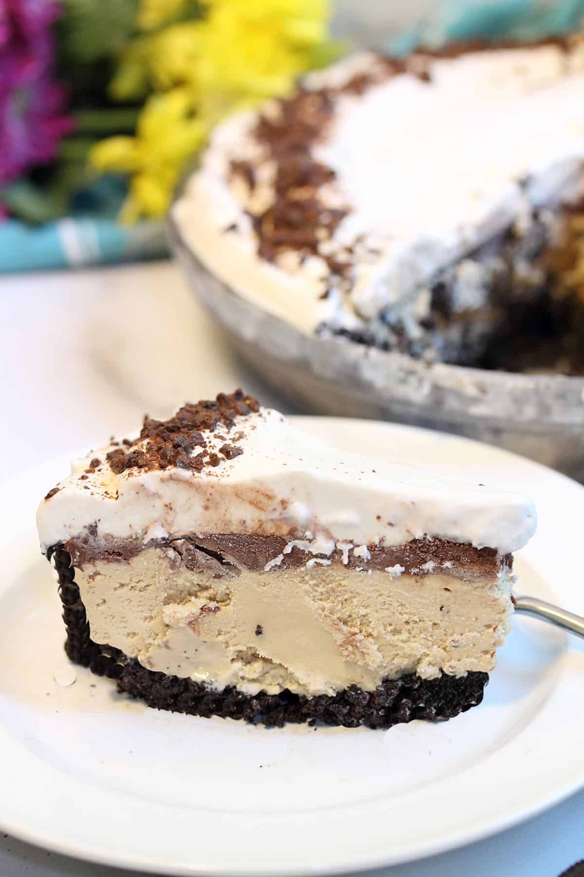 Slice of pie on white plate n front of whol epie and bunch of flowers.