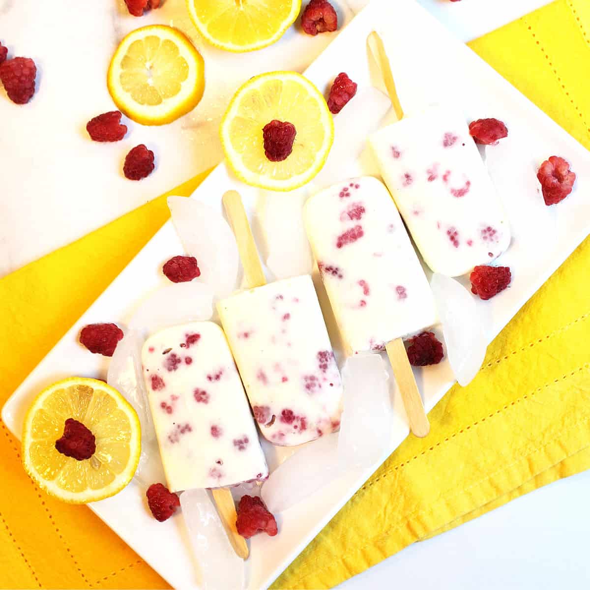 Overhead of lemon posicles on white platter with ice on yellow napkin.