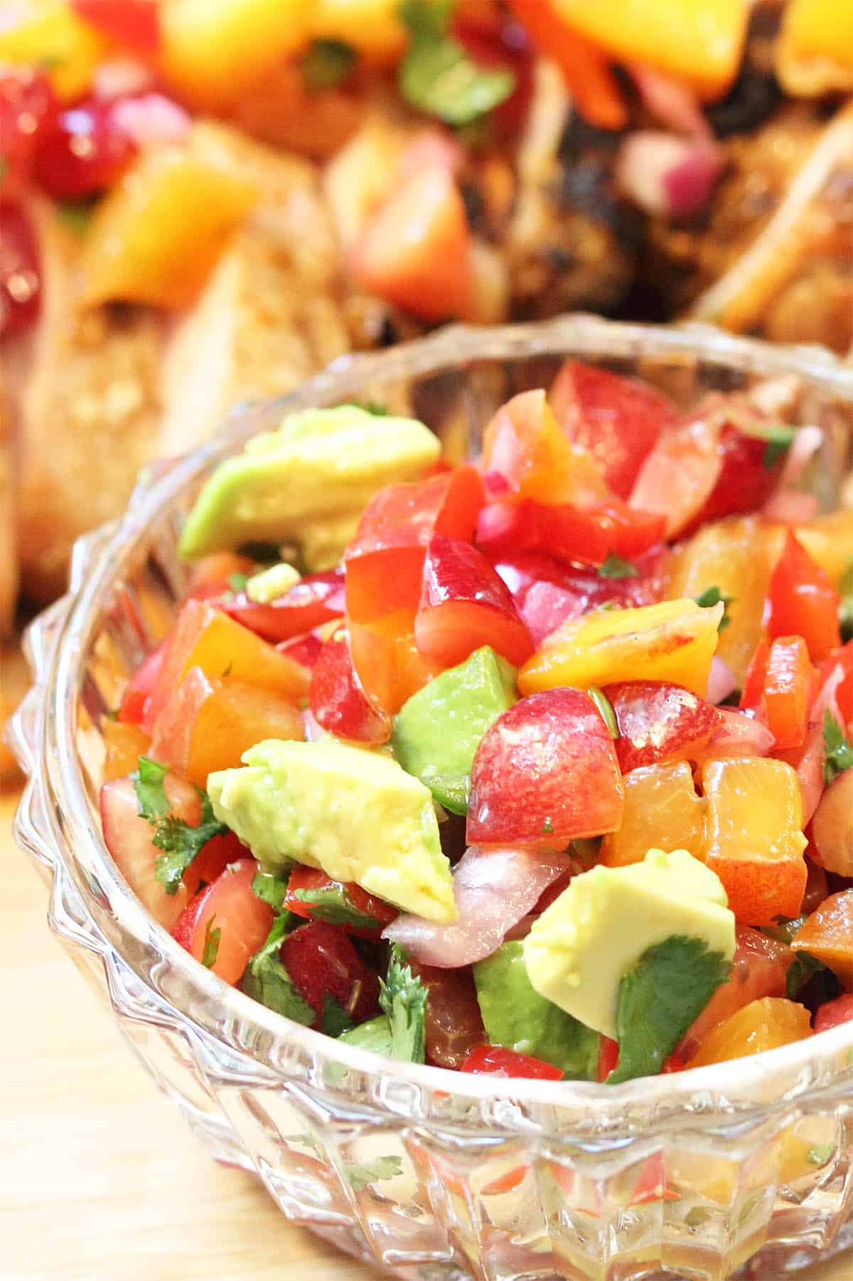 Closeup of salsa in glass bowl with pork in background.