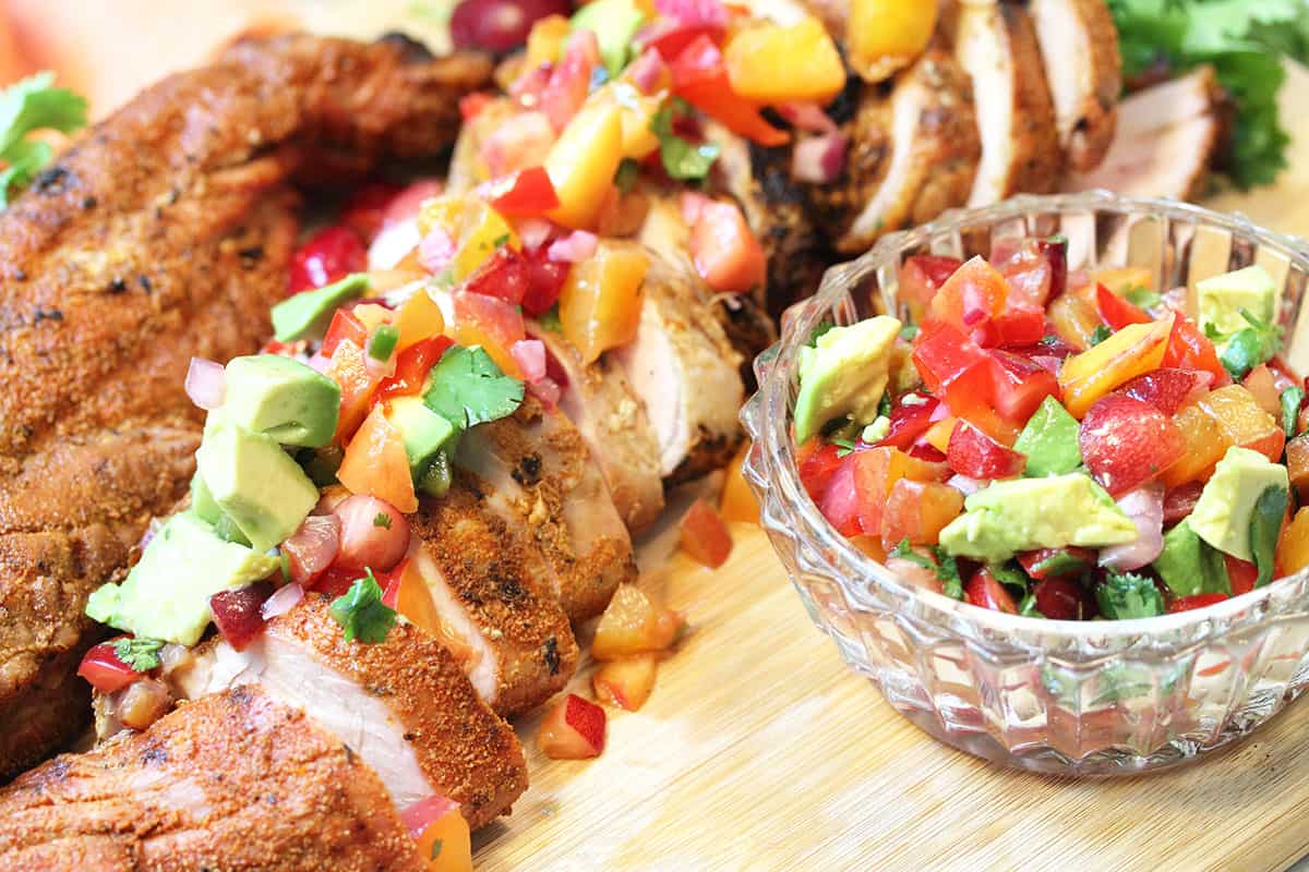 Glass bowl of peach salsa beside pork.