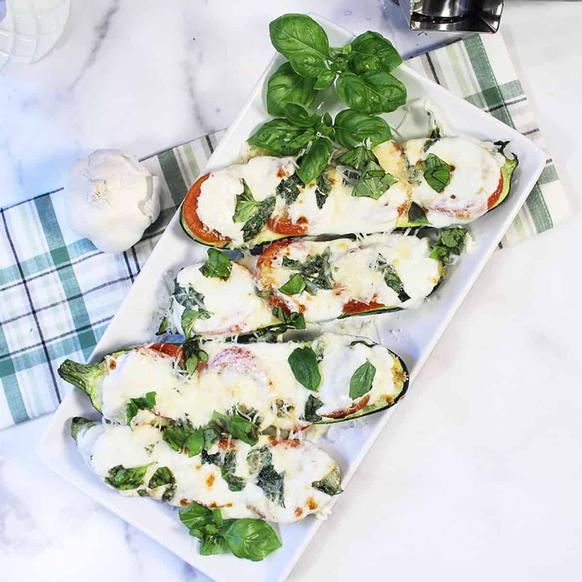 Zucchini boats on white plate with green plaid towel on side.