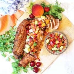 Peach salsa on grilled pork on wooden cutting board.