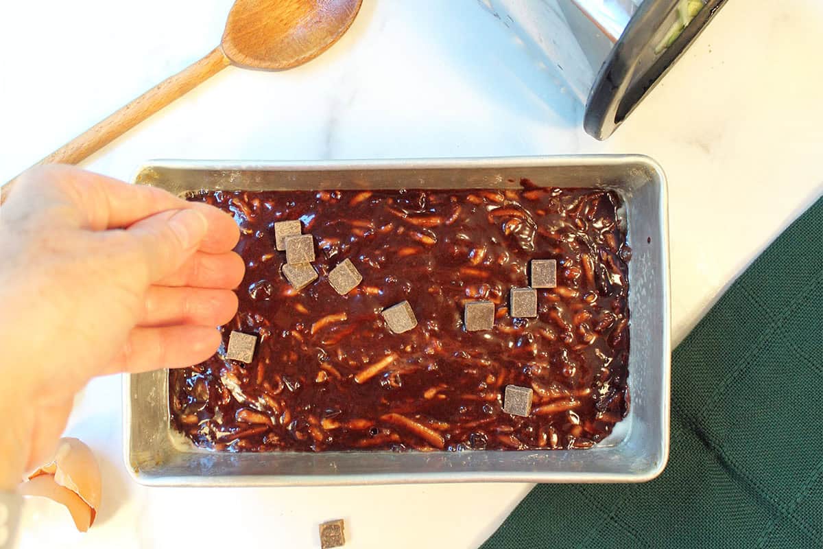 Scattering chocolate chunks over top of chocolate zucchini batter in baking pan.
