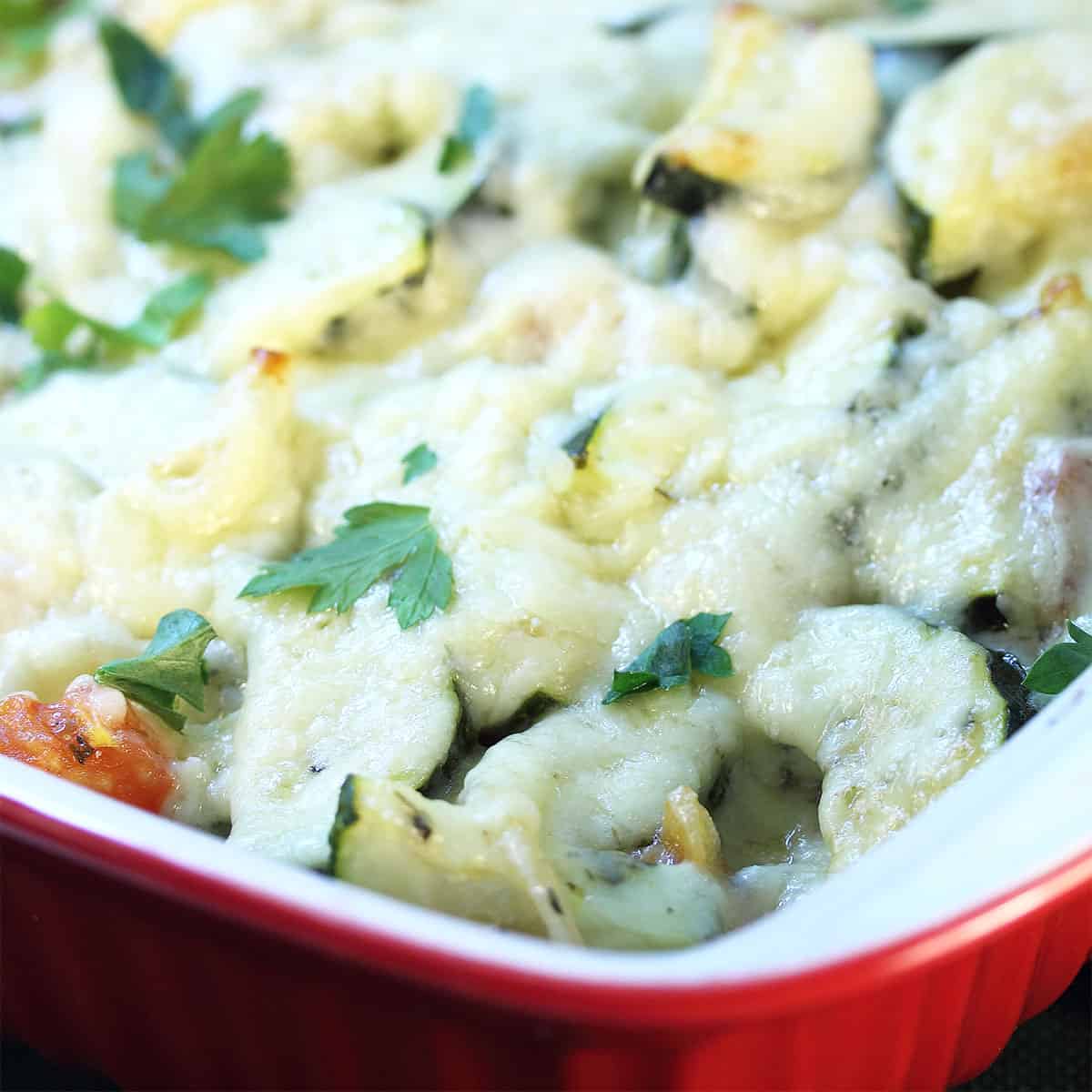 Closeup of cheesy topping on Cheesy Zucchini Casserole in red casserole dish.