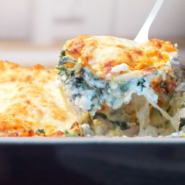 Lifting creamy white chicken lasagna with spinach from casserole.