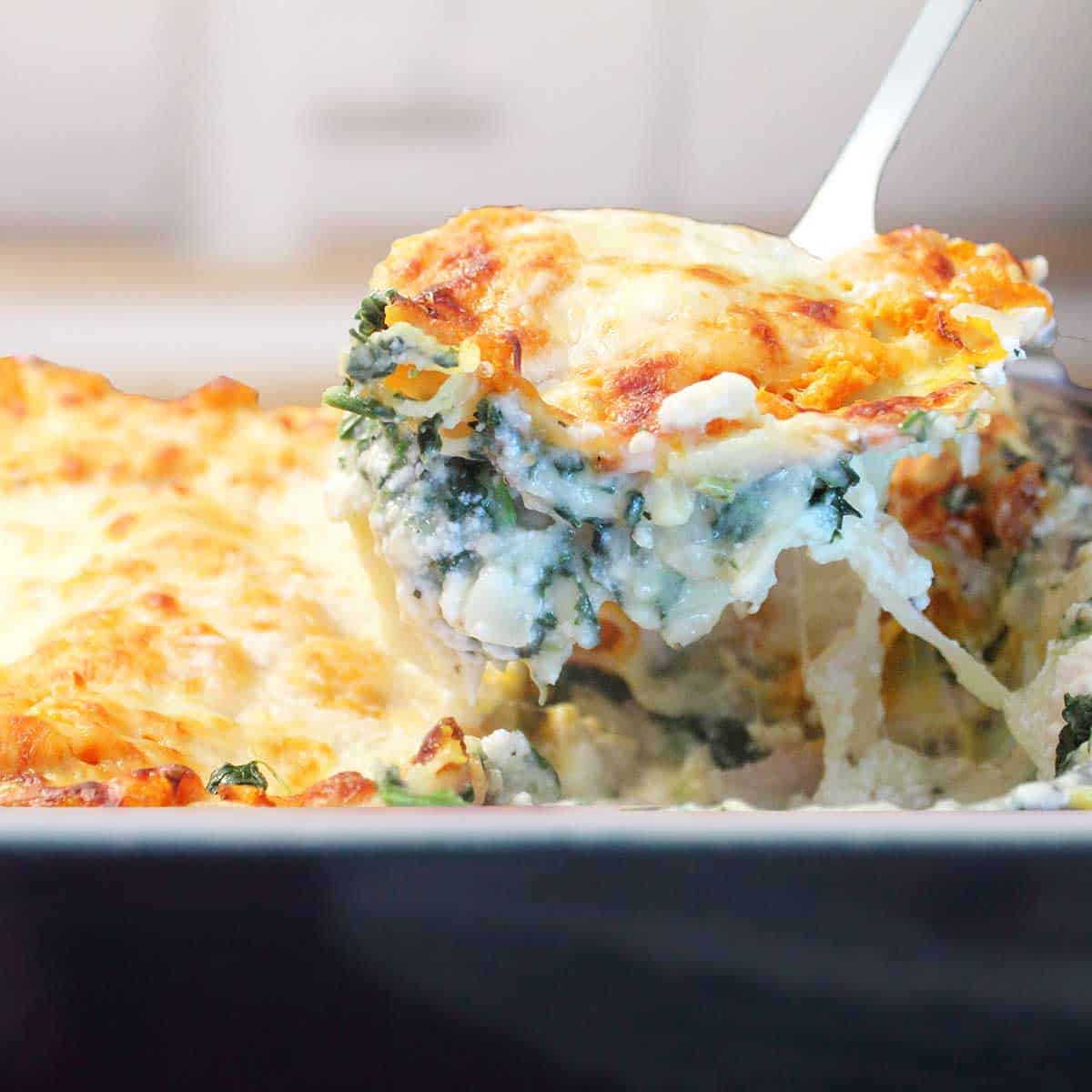 Lifting creamy white chicken lasagna with spinach from casserole.