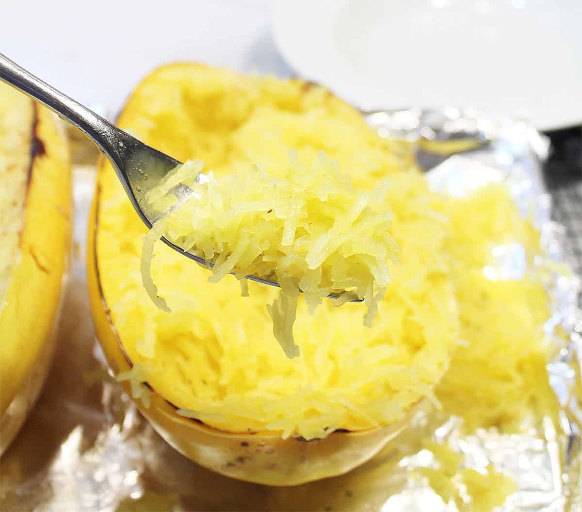 Forkful of spaghetti squash strands over cooked squash.