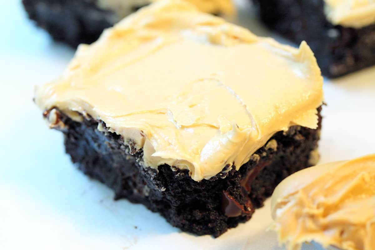 Peanut Butter Frosted brownie on white table with spoon of peanut butter.
