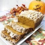 Sliced pumpkin bread on white platter with pumpkin in background.