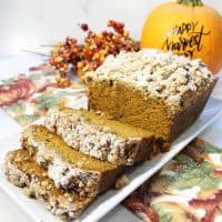 Sliced pumpkin bread on white platter with pumpkin in background.