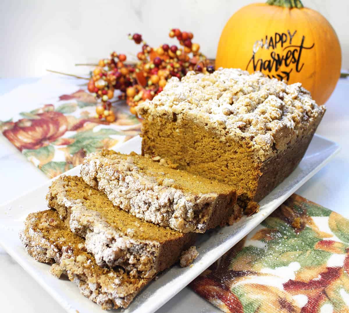 Sliced pumpkin bread on white platter with pumpkin in background.