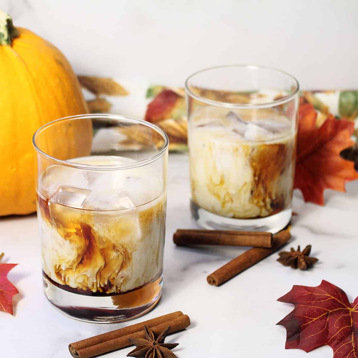 Two cocktails sitting on white table with fall leaves.