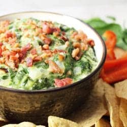 Closeup of bowl of dip with tortilla chips and red peppers around it.