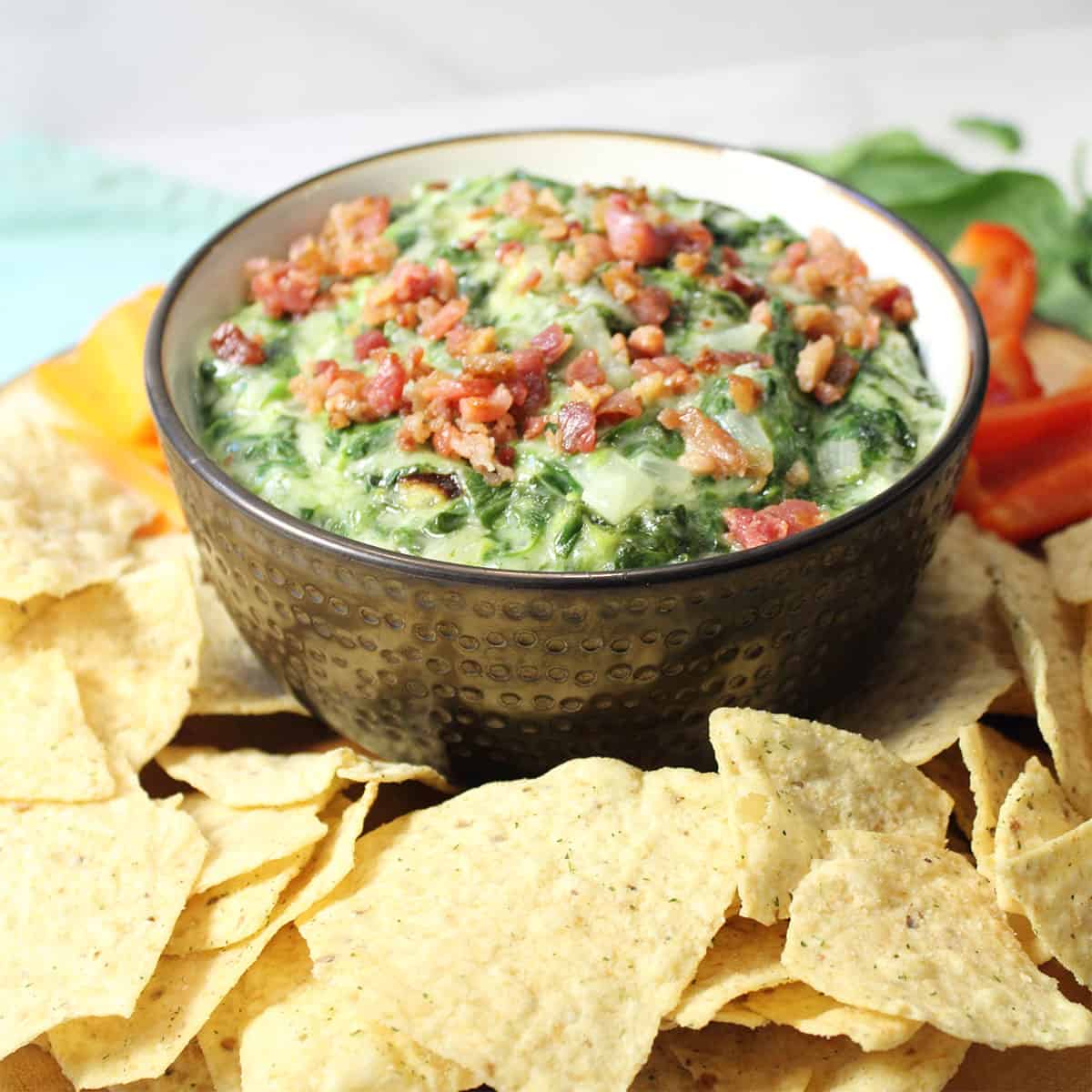 Dip in brown bowl on wooden circle with tortilla chips and dippers around it.