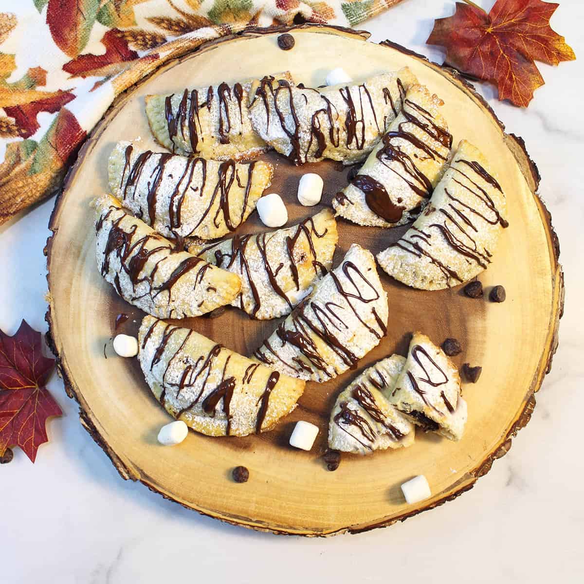 Overhead of chocolate drizzled empanadas on wooden board.