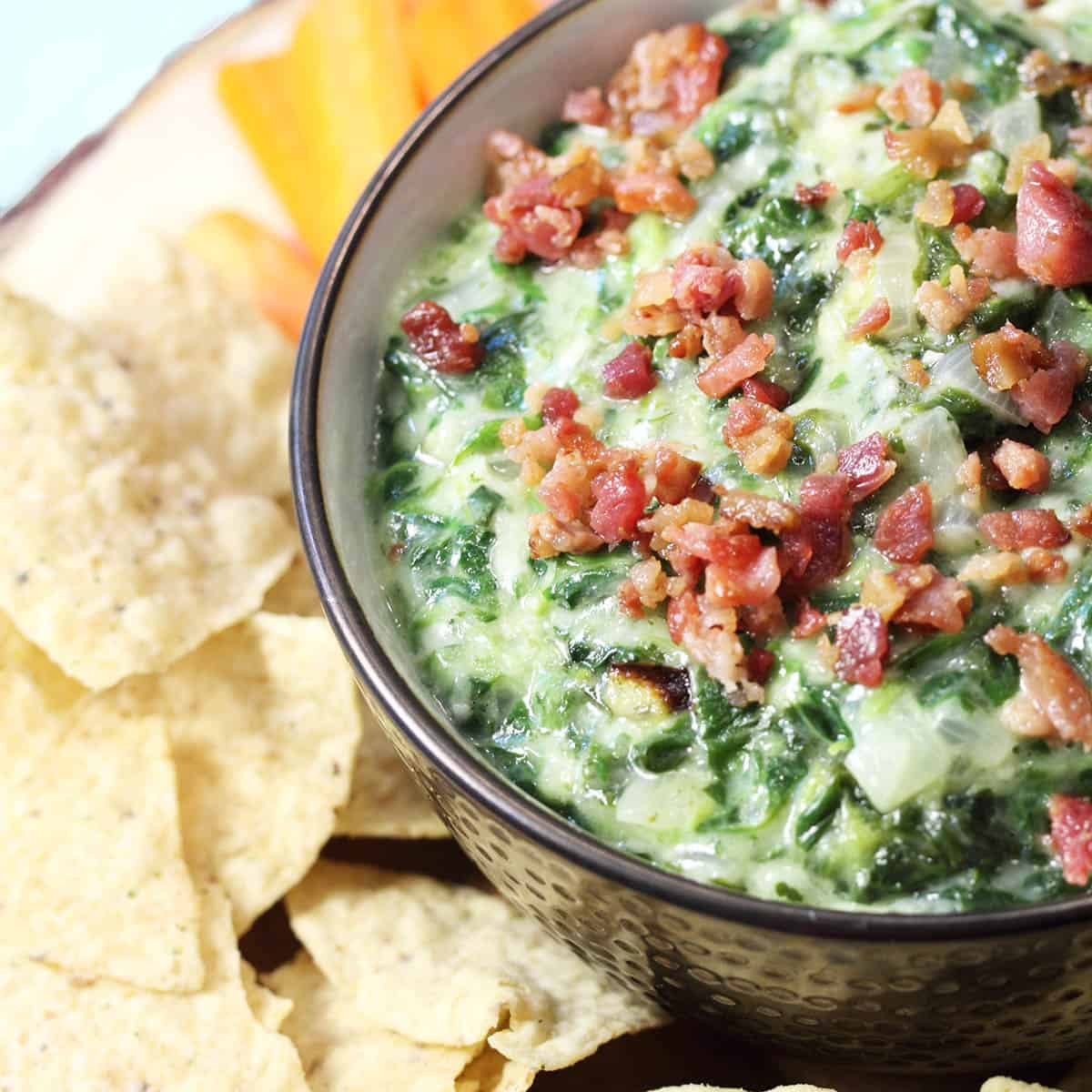 Overhead of partial bowl showing closeup of spinach and onions in cheesy sauce with tortilla chips.