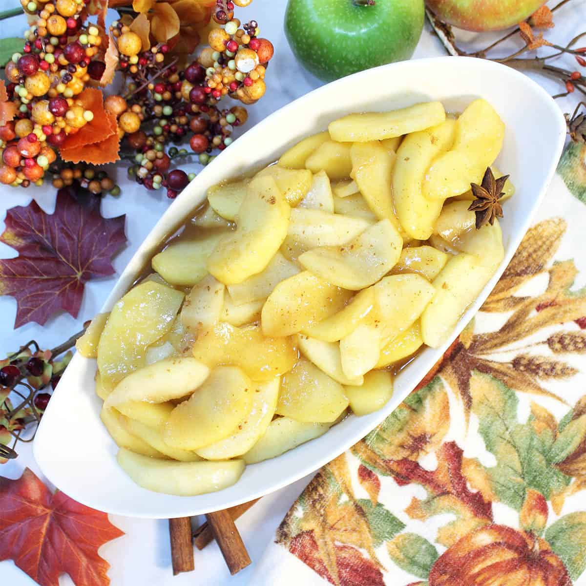 Overhead of serving bowl of apples with fall towel and leaves beside it.