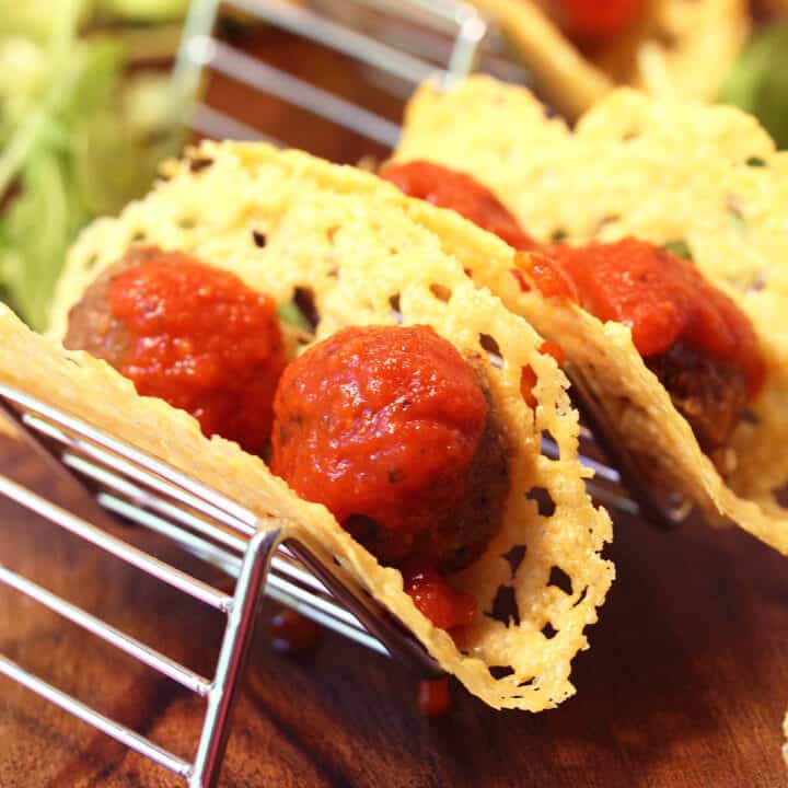 Sauce covered meatballs in cheese shells on taco stand.