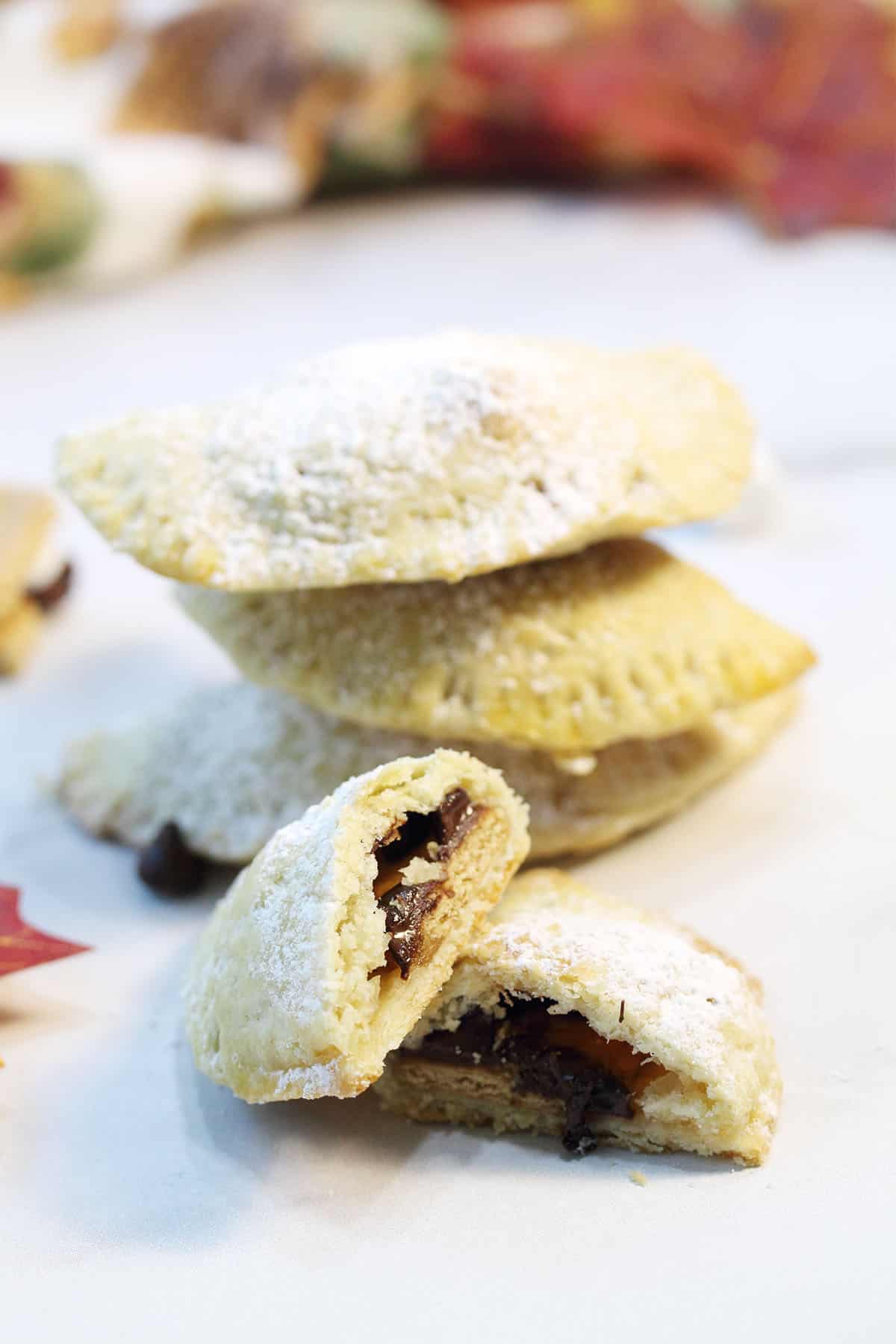 Stacked empanadas with a cut one in front of them on white table.