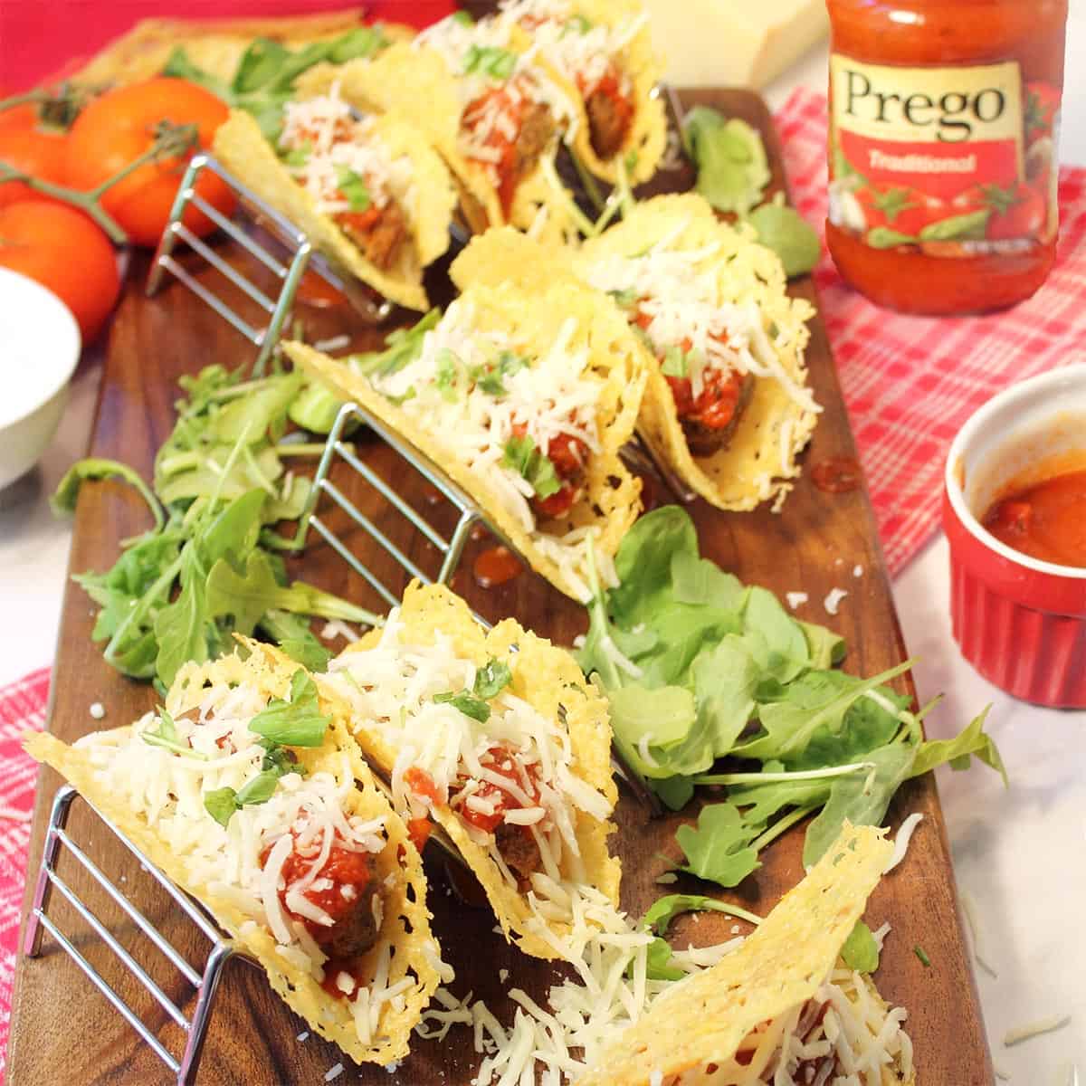 Tacos served in taco stands on wooden board with Prego sauce in background.