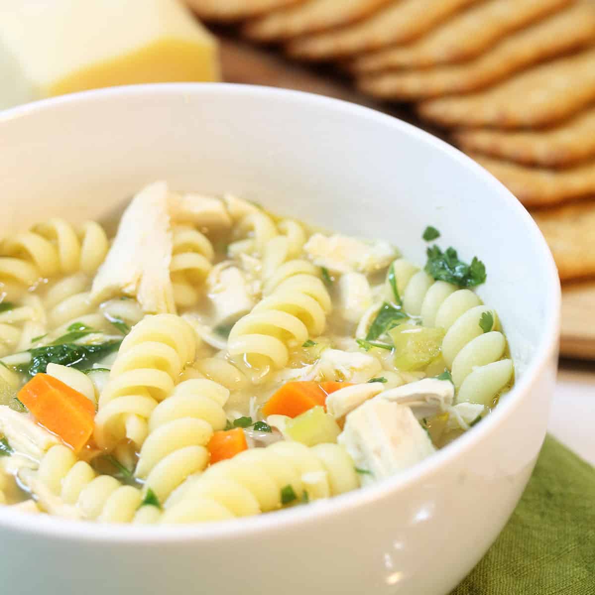 Bowl of chicken noodle soup in front of cheese tray.