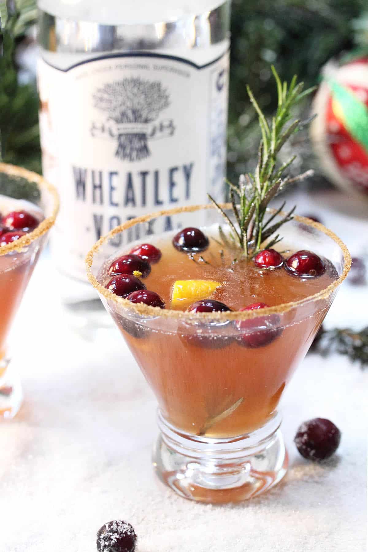 Garnished Christmas Berry cocktail in front of Wheatley vodka and greenery.