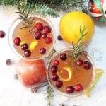 Overhead of cocktails on snow with orange apple and ornament around them.