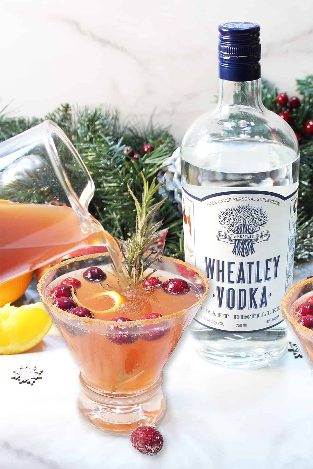 Pouring vodka cranberry cocktail into cinnamon sugar rimmed glass with Wheatley vodka bottle in back.