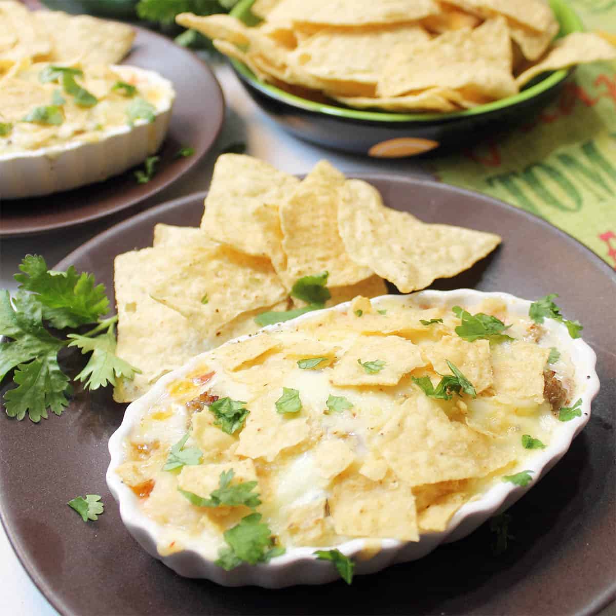 Baked breakfast ramekin on brown plate with extra tortilla chips in back.