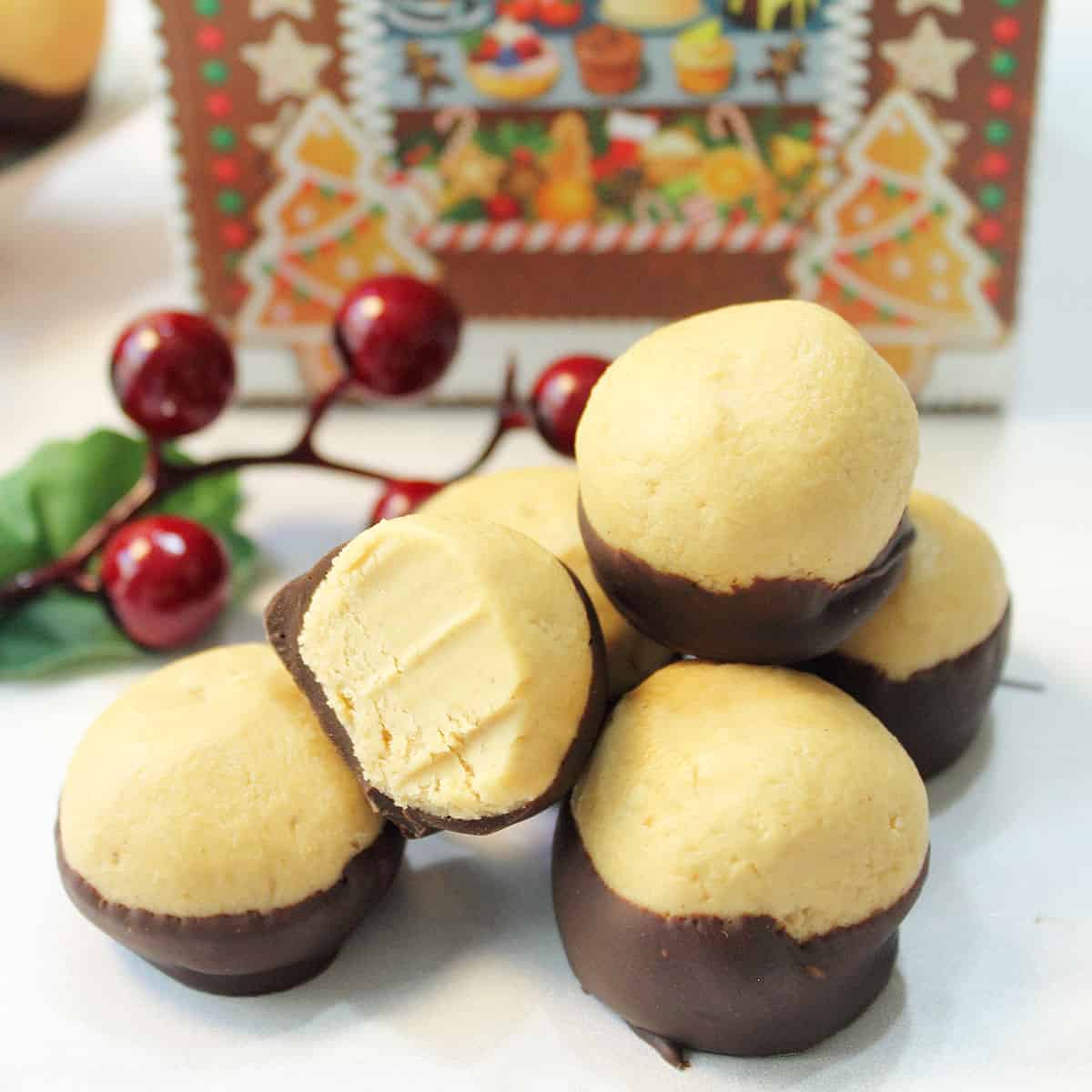 Closeup of group of buckeyes one with bite taken out on white table with holly berries in back.