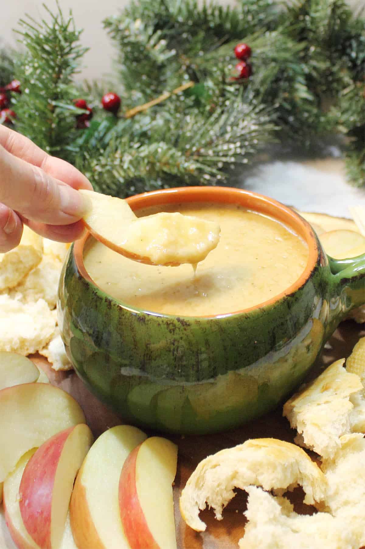 Dipping apple into Melting Pot Cheddar Cheese Fondue with greens in background.