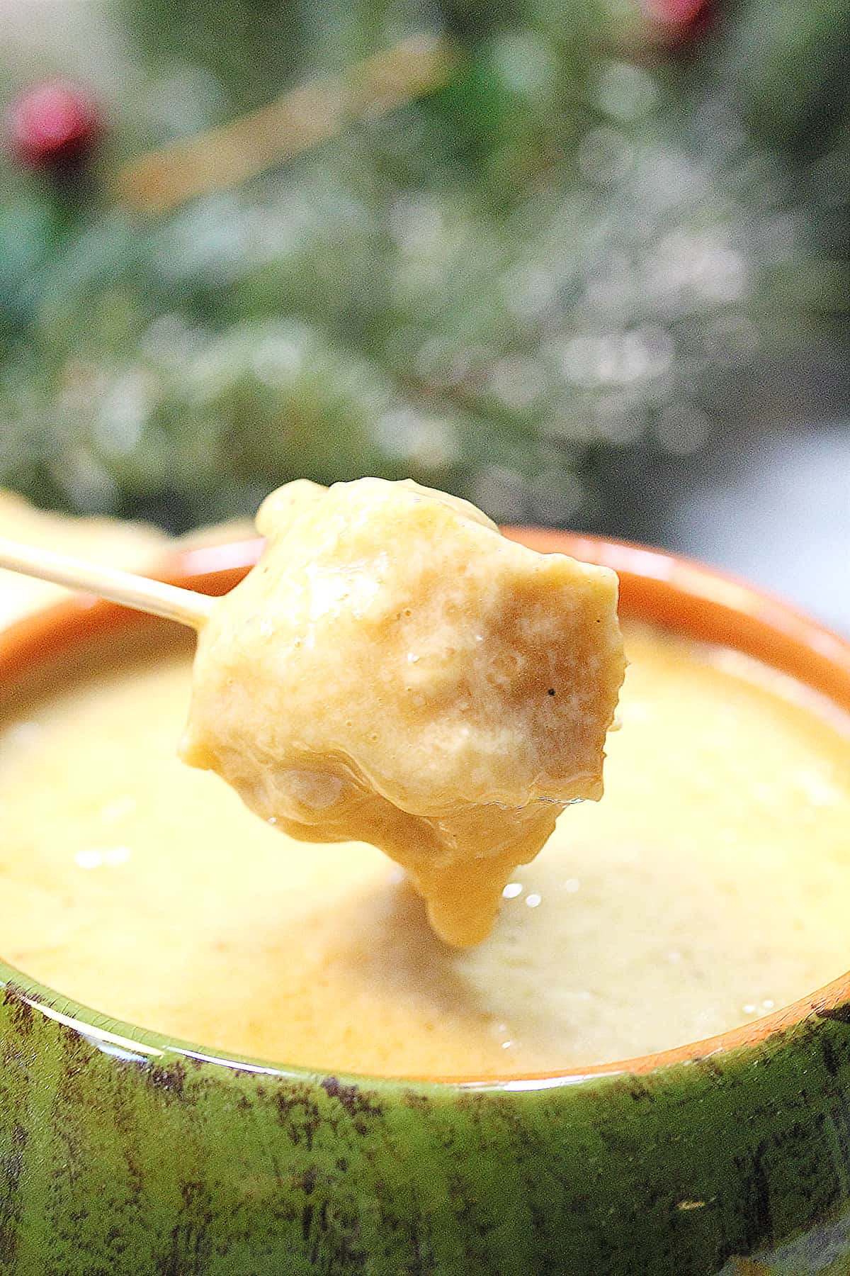 Closeup dipping bread into cheddar fondue.