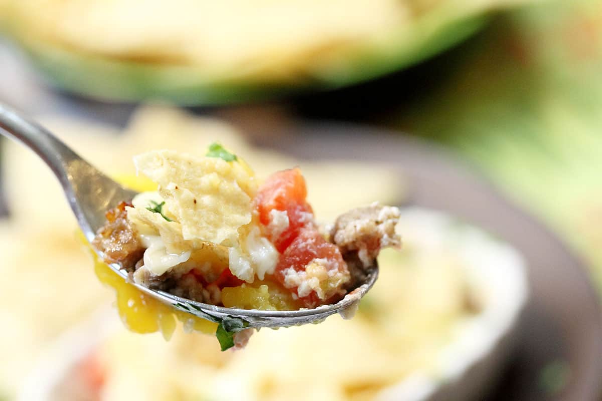 Spoonful of eggs sausage tomatoes with tortilla pieces on top.