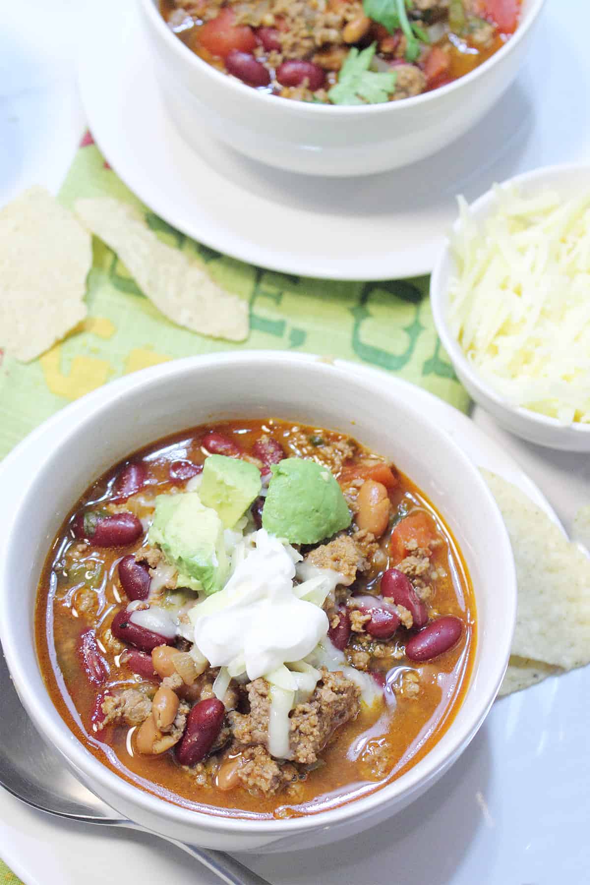 Two bowls of taco chili with cheese and chips.