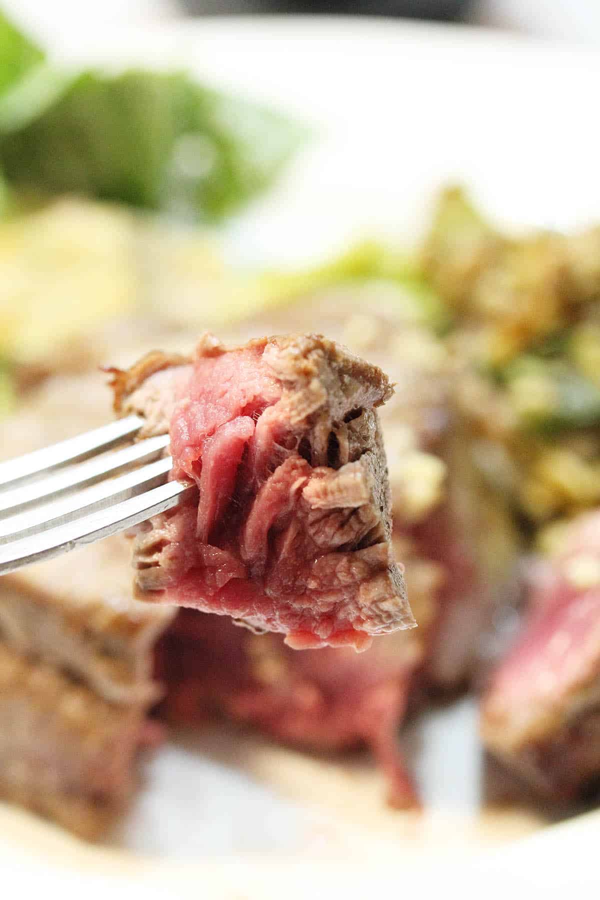 Bite of medium rare steak on fork over plate.