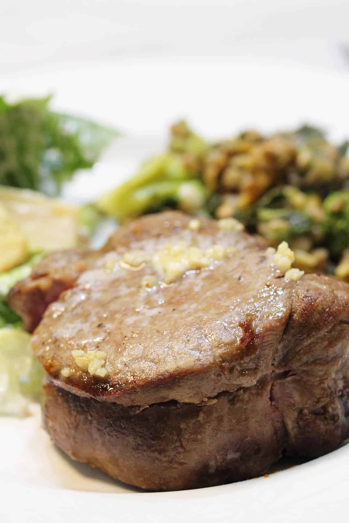 Closeup of cooked filet mignon on white plate.