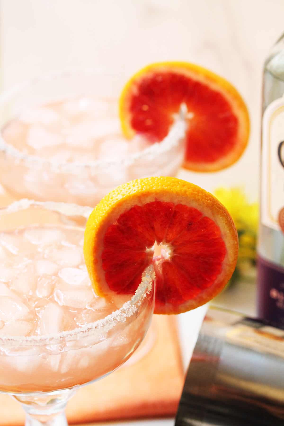 Closeup of partial top of cocktail glasses showing sugar rim and blood orange slice garnish.