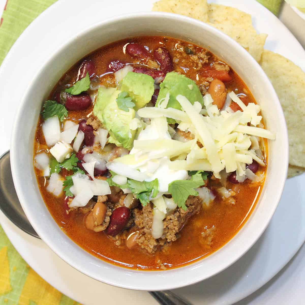 Overhead of white bowl of chili with cheese avocado and sour cream.