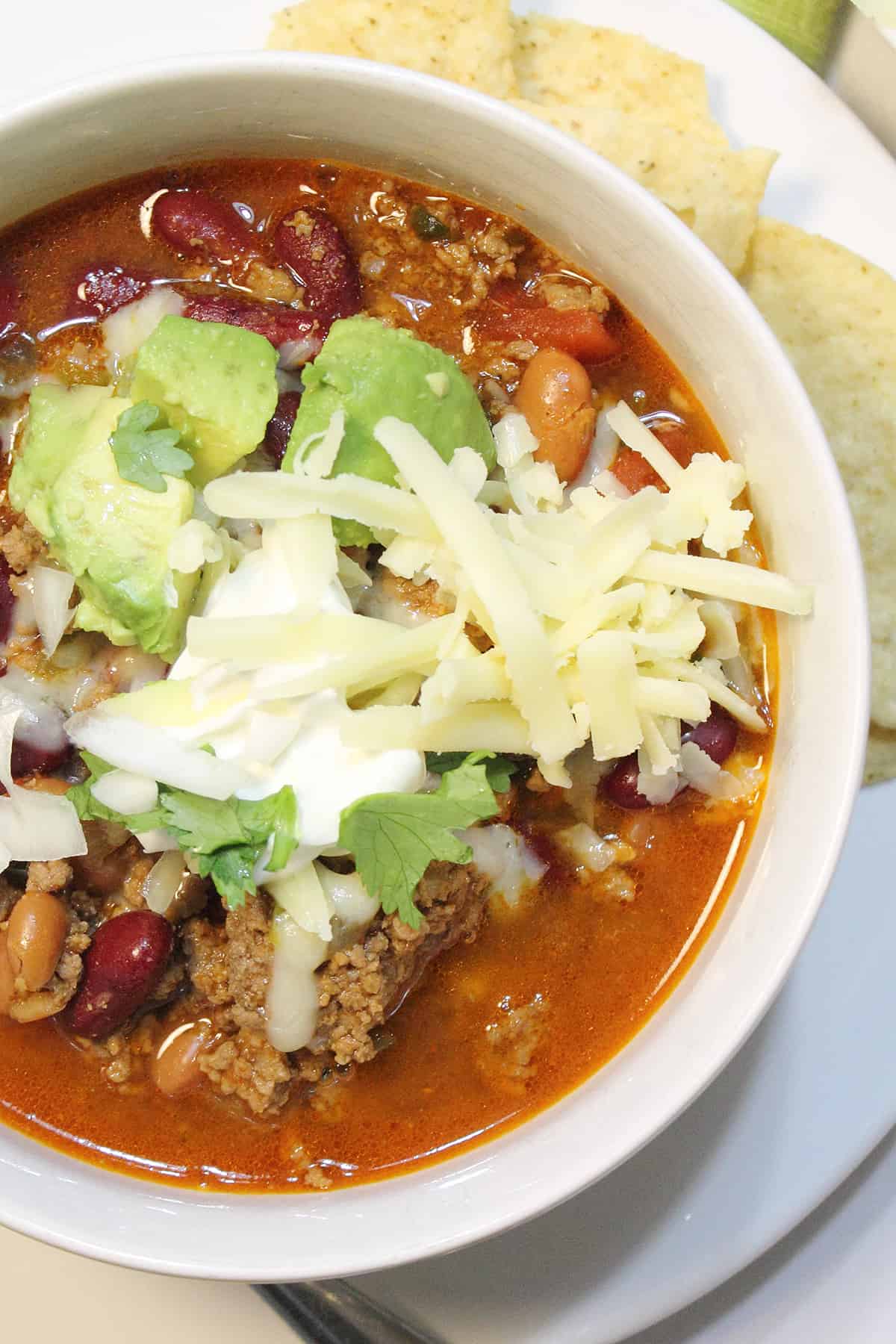 Overhead of partial bowl of slow cooker taco chili topped with cheese, avocado and sour cream.