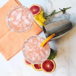 Overhead of two cocktails surrounded by blood orange slices orange napkin and shaker.