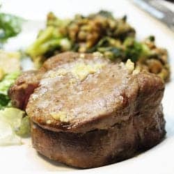 Steak dinner complete with salad and vegetable on white plate.