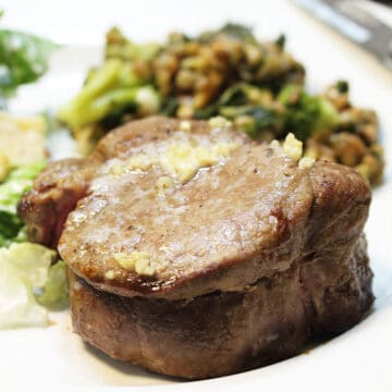 Steak dinner complete with salad and vegetable on white plate.