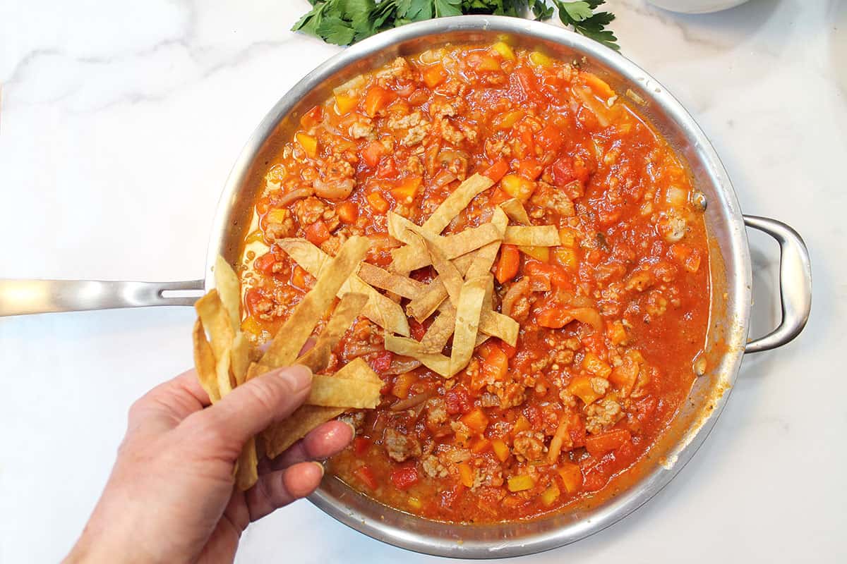 Tossing crispy corn chips on rich tomato sauce based turkey chili.