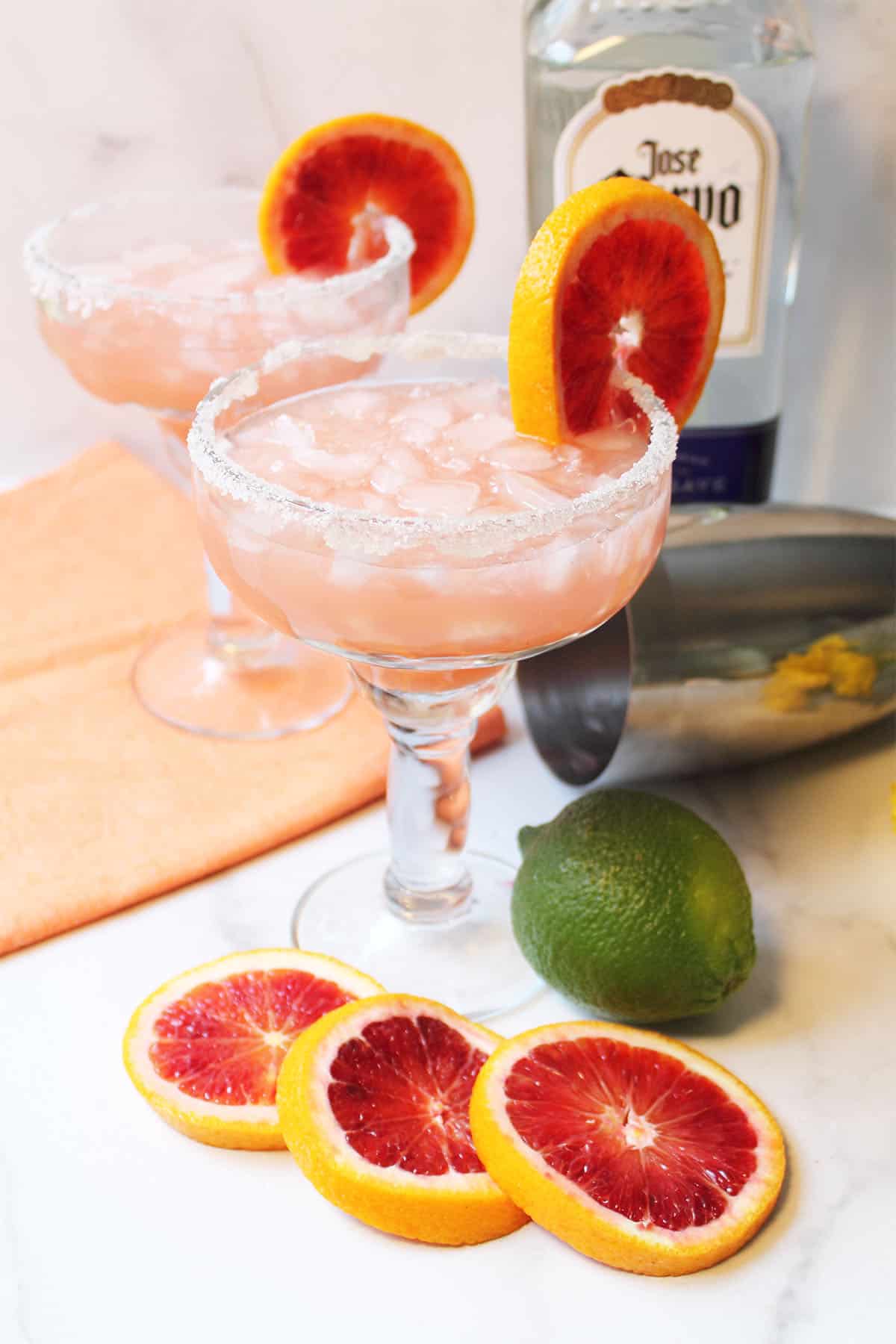 Two cocktails with blood orange garnish on white table.