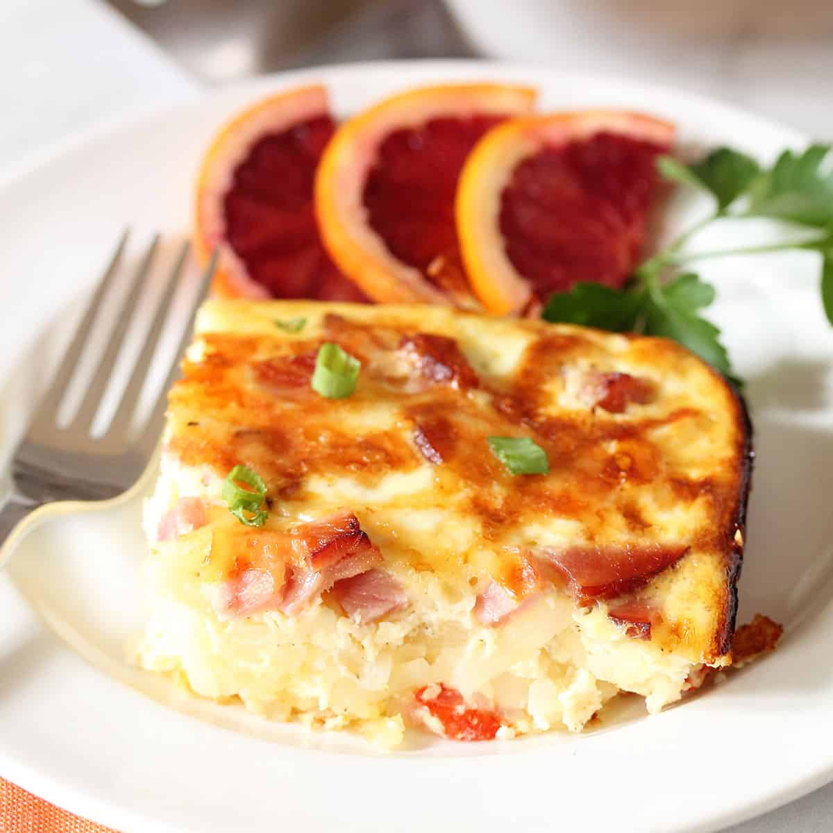 Slice of casserole on white plate with fork beside it.