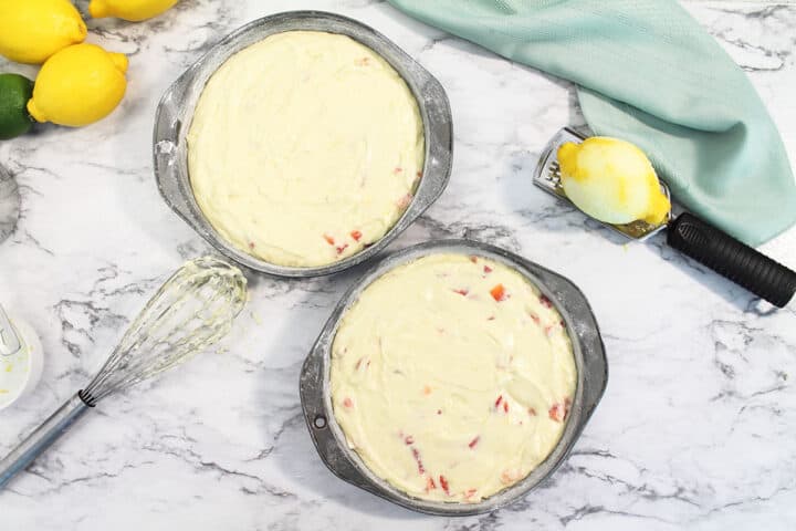 Cake batter poured into cake pans on white marble table. Ready to bake.