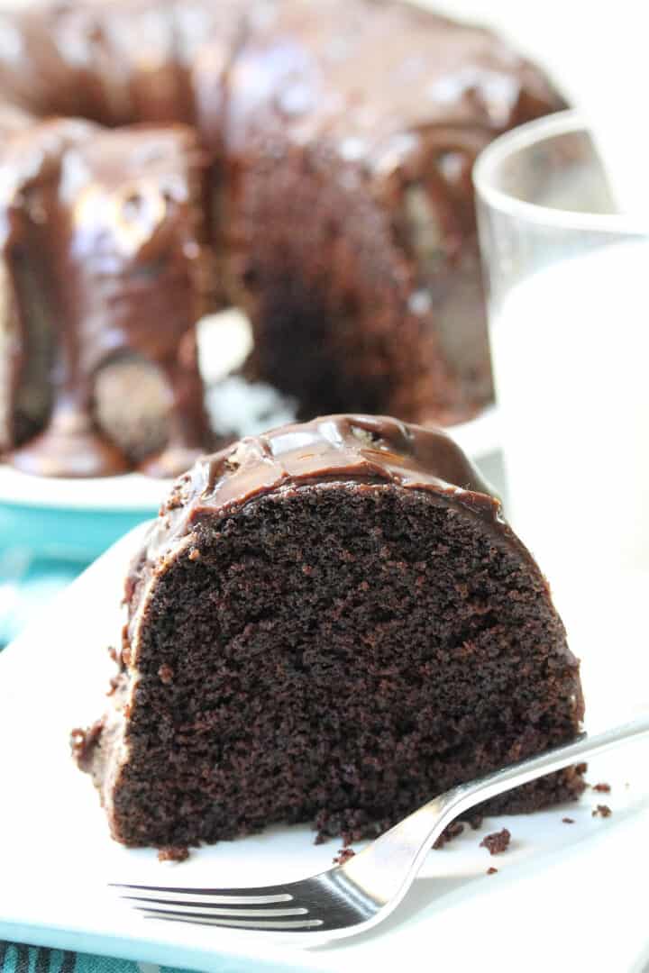 Slice of moist chocolate pound cake on white plate with fork and glass of milk.